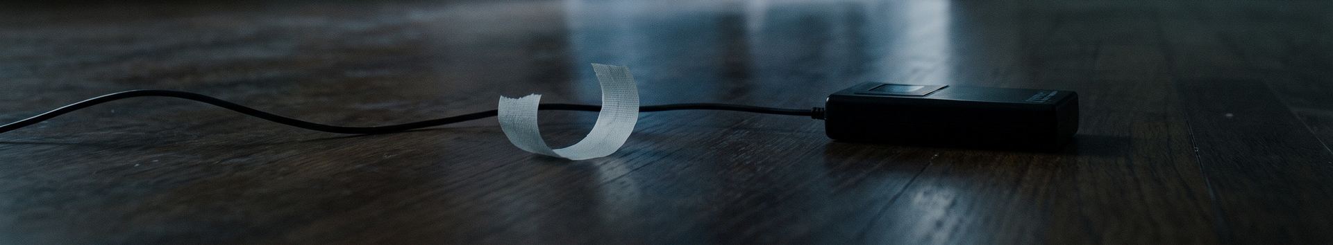 A wire, a curl of tape and a small transmitter lying on a dark wooden floor.